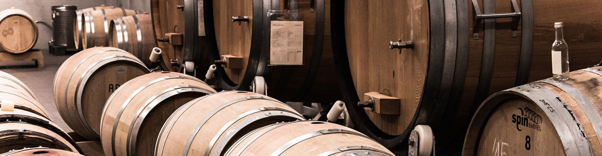 A winery cellar room with small and large oak wine barrels and winemaking equipment.