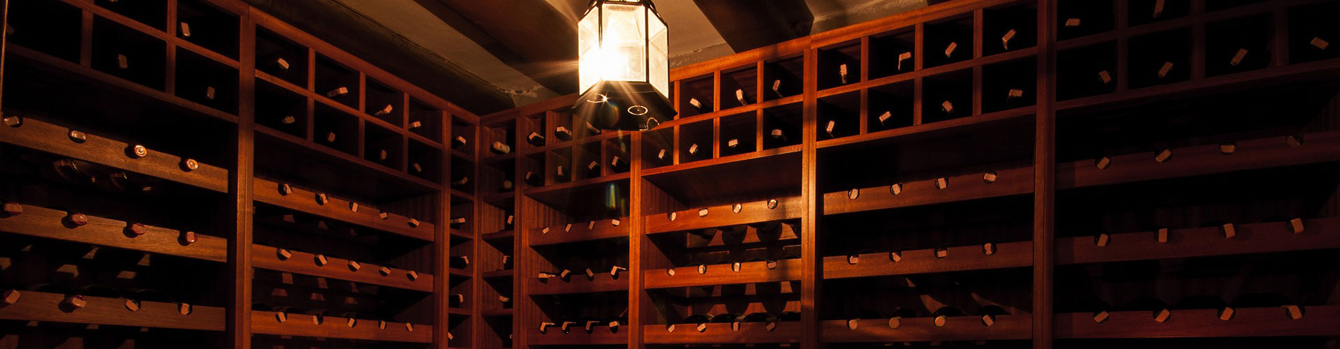 A softly lit wine cellar filled with wine bottles on wooden wine racks.