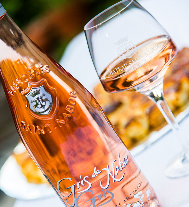 A bottle and glass of Chateau Saint Nabor Gris de Nabor Rosé wine on a table.